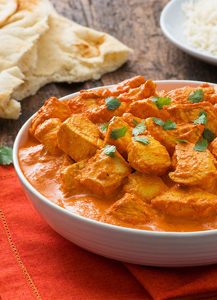 A bowl filled with steaming Chicken Tikka Masala served with a side of naan and rice.