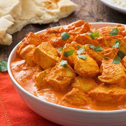 A bowl filled with steaming Chicken Tikka Masala served with a side of naan and rice.