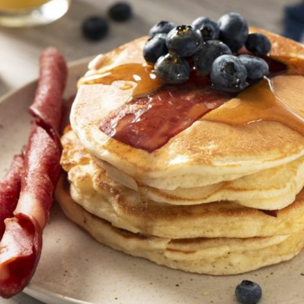A stack of fluffy flapjacks served with syrup, fresh blueberries, and Breakfast Chicken Strips