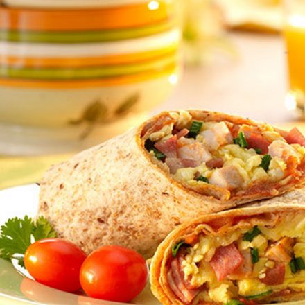 A sunny breakfast table setting with orange juice and aplated breakfast burrito served with fresh vegetables