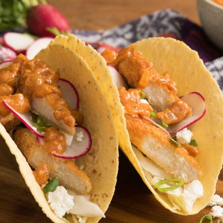 Two butter chicken tacos topped with fresh radish slices and sauce.