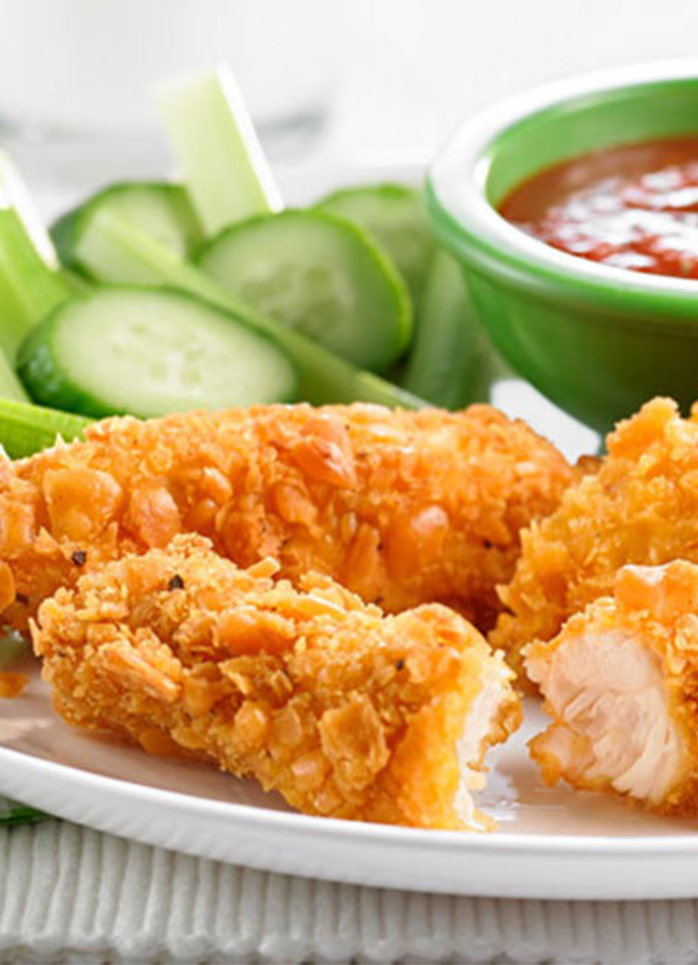 A plate of Chicken strips coated with cheesy fish crackers, served with fresh veggies and dipping sauce