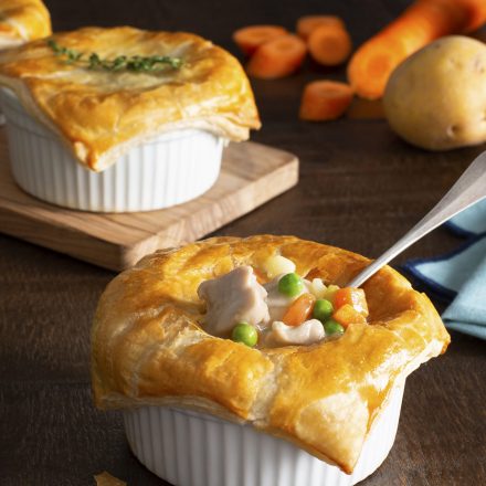 A tray of 3 mini Chicken Pot Pies with golden crusts in white ramekins. The first pie has a spoon in it, showing the chicken and vegetable filling.