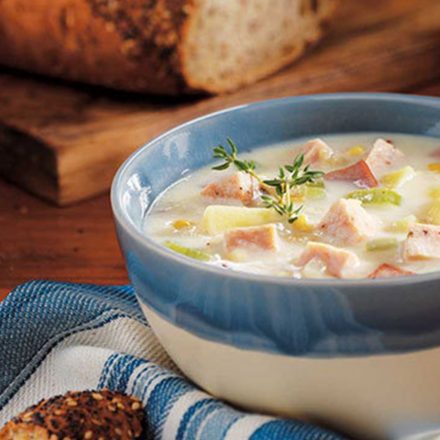 A bowl of Chicken & Corn Chowder on a table with freshly baked bread.