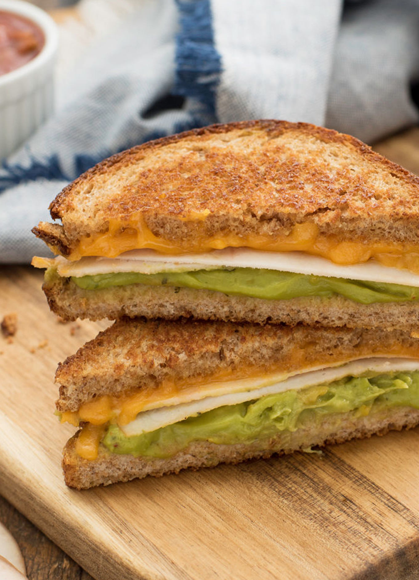 A cross section of a Chicken Guacamole Grilled Cheese on a wooden cutting board showing the deli slices, layer of guacamole, and the melted cheese