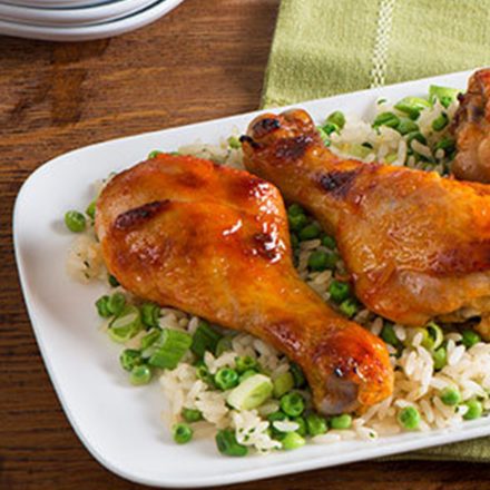 A tray of roast drumsticks with a honey and Sriracha glaze served on a bed of rice and peas.