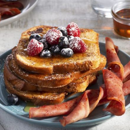 A stack of French Toast topped with syrup and fresh berries, served with a size of Breakfast Chicken Strip Twists