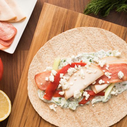 Une tortilla au poulet méditerranéen sur une planche à découper en bois accompagnée d’ingrédients frais.