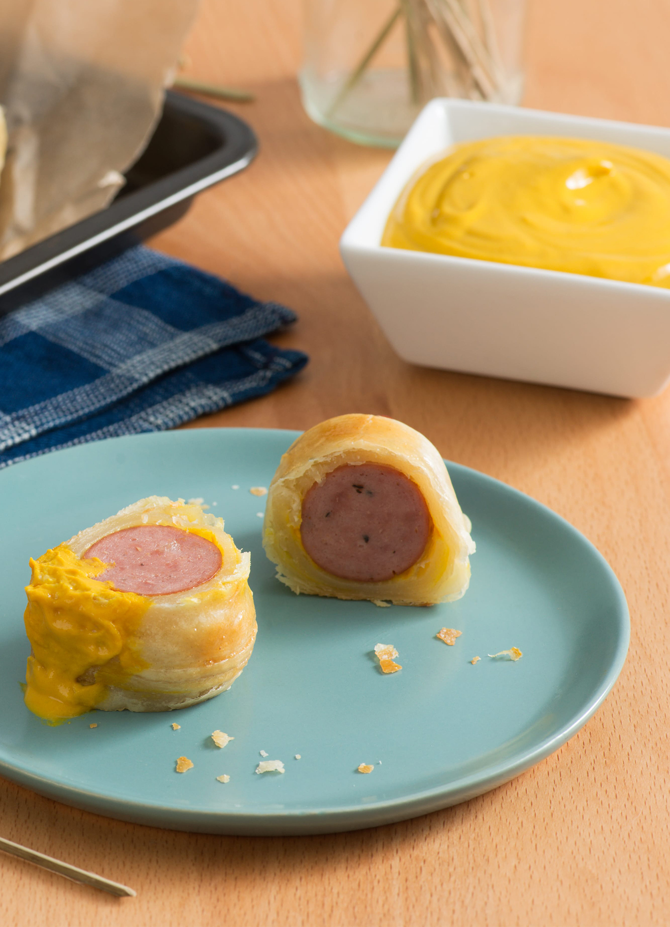 A tray of Mustard-y Sausage rolls with golden flaky pastry, and a ramekin of mustard for dipping.