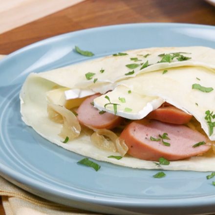 A crepe filled with Halal Chicken Sausage, brie cheese, and sauteed onions plated on a breakfast table.