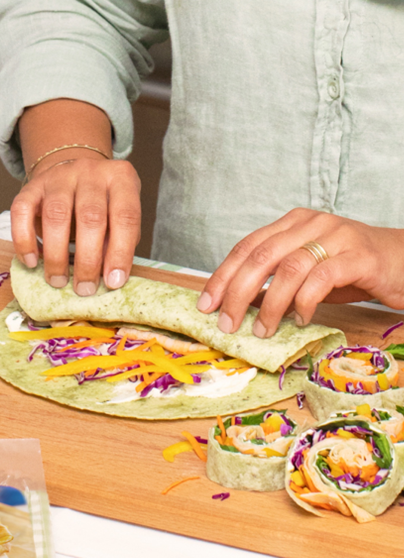 Une personne confectionnant des roulés végétaux de spirales arc-en-ciel accompagnés de légumes frais et de tranches de rôti de poulet halal.